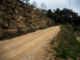 imagen de un camino de tierra con una pared de piedras a un lado y hierba verde al otro, con el...