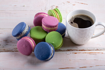 Lots of colorful macaroons and a cup of coffee on a wooden table