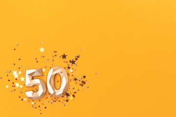 Golden number fifty and shiny stars confetti on a yellow background. Festive compisition with copy...