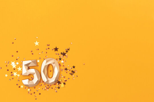 Golden number fifty and shiny stars confetti on a yellow background. Festive compisition with copy space.