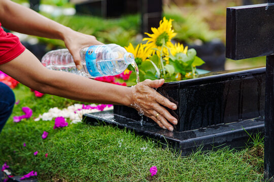 Woman cleaning gravestones while visiting deceased family members using bottled water on sunny day