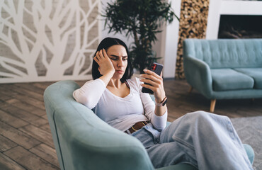 Obraz premium Tired female watching boring video on smartphone