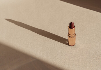 Dark red lipstick on beige neutral background, minimalist make-up aesthetic, copy space