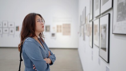 Asian Woman wearing eyeglasses looking artworks on the wall in art gallery