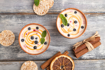 Yoghurt with bilberry and caramel in clay bowl on gray wooden, top view