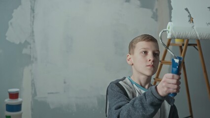 Teenager paints on glass with white paint using a roller. Young boy holds a roller in his hands and looks at the glass intently. Concept of repair, finishing works, interior design.