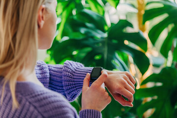 woman in the purple sweater checks the time on her wristwatch with palm plants on background
