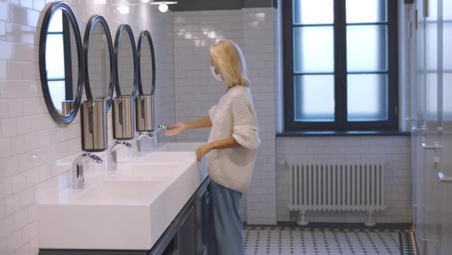 Senior woman in safety mask washing her hands in a public toilet. Realtime