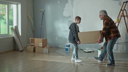 Grandpa and grandson are carrying heavy cardboard box. An elderly man and a teenager are preparing for repairs in the apartment. Concept of repair, assistance and family relationships.