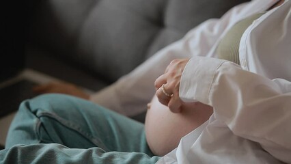 Close up unrecognisable pregnant woman touches and caress her big belly. Girl uses laptop on sofa, at home remotely works, communicates online, brows social media. Business and pregnancy concept