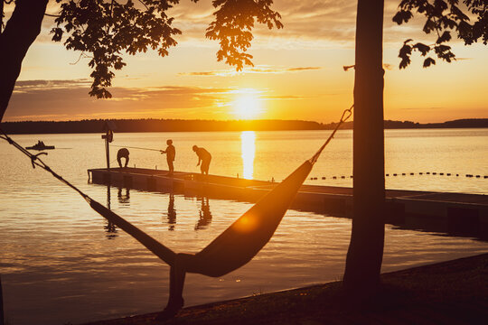 Summer sunset by the calm lake with people relaxing on jetty,  fishing, lying on hammoc, copy space