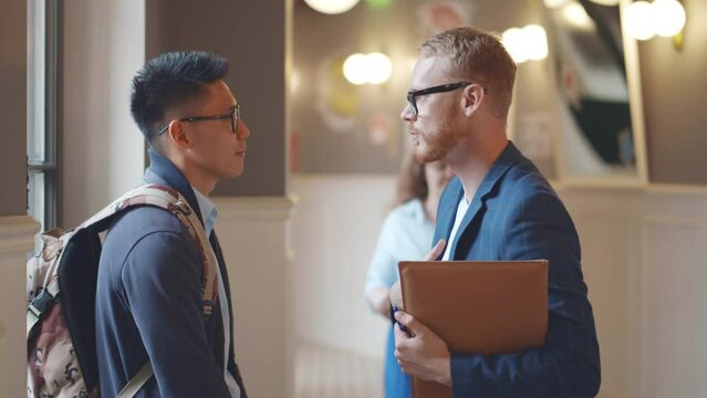 Talking male teacher and asian man college student in corridor. Realtime