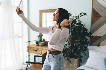 Cheerful woman standing and taking selfie on smartphone