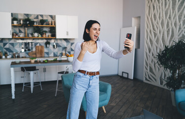 Glad female taking selfie on phone in kitchen - Powered by Adobe