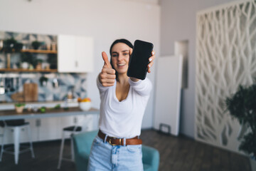 Satisfied lady demonstrating screen of cellphone in kitchen