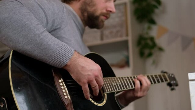 Playing the guitar. Strumming black acoustic guitar. Musician plays music. Man fingers holding mediator. Male hand playing guitar neck in dark room. Unrecognizable person rehearsing, fretboard closeup