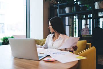 Busy woman sitting at table with documents and laptop in cafe