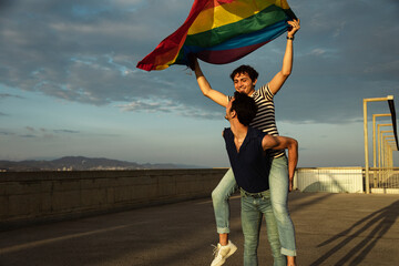  Happy young couple with rainbow flag. Two men enjoy outside.