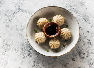 Chinese steamed dumplings in a plate with soy sauce and chopsticks on a gray concrete background top view