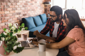 Latino or indian man and woman couple use their laptop in the living room to make video calls. Video call and online chat with family