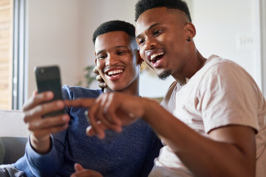 Happy Young Gay Male Couple Using Smart Phone At Home