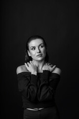 Fototapeta premium Sexy looking woman with dark clothes and wet hair style studio portrait in black background. Grace pose and seductive look of the model away. Hands placed on shoulders. Black and white image