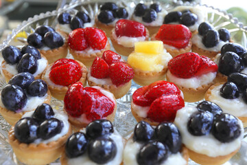 Colored mini tarts with strawberry, ananas and grapes on a table.
