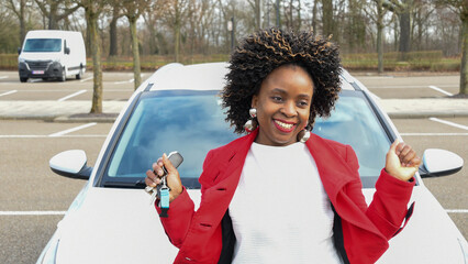 a cheerful african american woman stands next to the car and holds the keys © Ekaterina