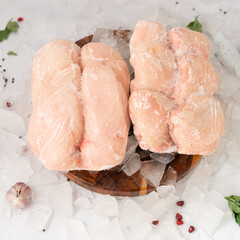 frozen raw chicken breast with vegetables on the ice on wooden board on the.gray rock background