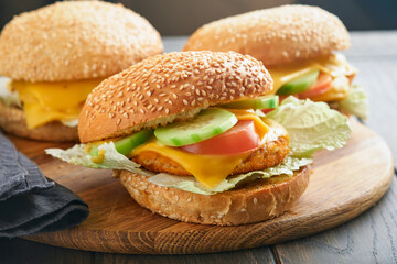 Homemade fish burger with vegetables on rustic wooden board. Side view, close up. Menu.