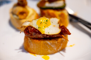 White board with typical snack of Basque Country, pinchos or pinxtos skewers with small pieces of bread, courgette, sea food, eggs, cheese, served in bar in San-Sebastian or Bilbao
