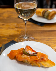 Board with typical snacks of Basque Country, pinchos or pinxtos, skewers or small piece of bread with toppings, served with glass of txakoli wine in bar in San-Sebastian or Bilbao, Spain