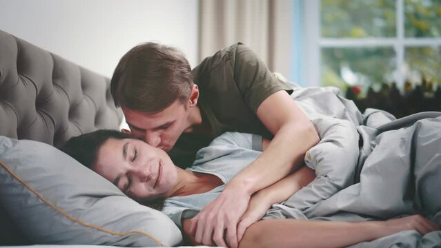 Young man wake up and kiss sleeping wife in bed. Realtime