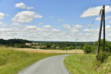 Fototapeta na wymiar Route secondaire de campagne entre les végétation et champs de blé près du Puy de Versac au Périgord Vert 