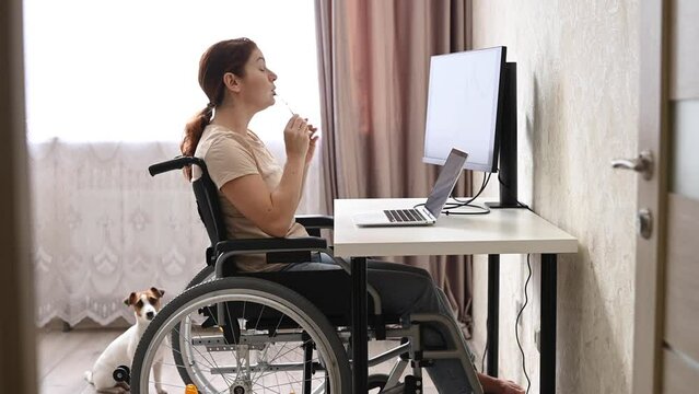Caucasian woman in a wheelchair typing with a laptop from home. Remote work for people with disabilities.