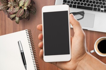 Hand holding a modern smartphone on office desk background.