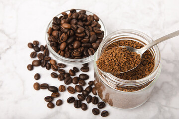 Fototapeta na wymiar Instant coffee beans in a glass jar on a white marble background. Hot drink ingredients. Instant coffee on the table. Espresso. Place for text. Place to copy. Banner.