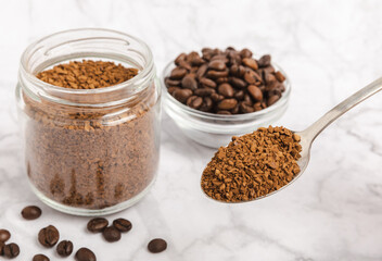 Obraz na płótnie Canvas Instant coffee beans in a glass jar on a white marble background. Hot drink ingredients. Instant coffee on the table. Espresso. Place for text. Place to copy. Banner.