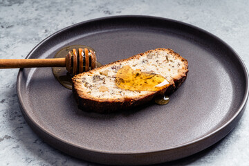 Slice of cake with walnuts and honey dipper on plate on gray background, close up