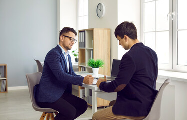 Legal services. Focused young businessman signing agreement with qualified lawyer during meeting in office. Male lawyer explains terms of contract and shows his client where signature is on document.