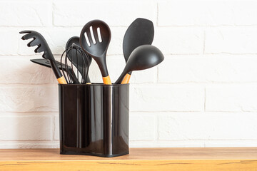 Kitchen utensils, cooking tools in black container near white wall.