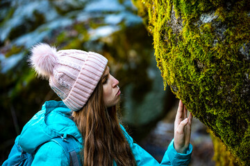 Beautiful girl in blue jacket touch and observe green moss covered rock in Yosemite National Park, California, USA. Bond with nature motive.