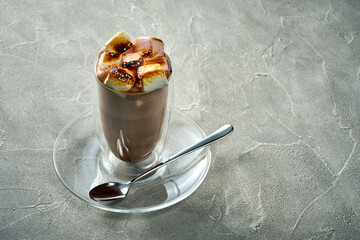 Cocoa or hot chocolate in a transparent glass with burnt marshmallows on a concrete background
