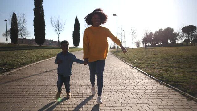 african american mother and son running hand in hand in park