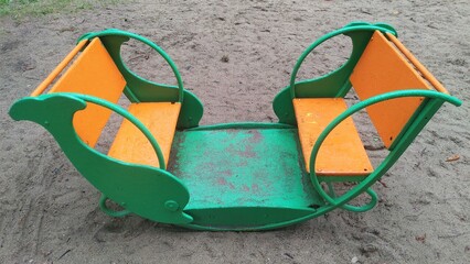 There are children's swings on the sandy pad. The body is made of metal, and the seats and backs...