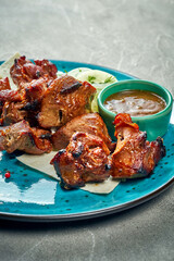 Grilled pork shish kebab in a blue plate with sauce and pita bread. Close-up.
