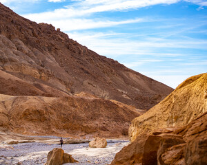 hiker girl walking through golden canyon in death valley national park, california, usa; little silhouette of woman in front of large mountains in the desert