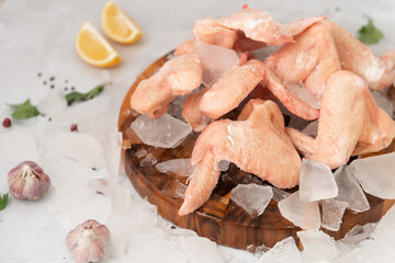 frozen raw chicken wings with vegetables on the ice on wooden board on the.gray rock background