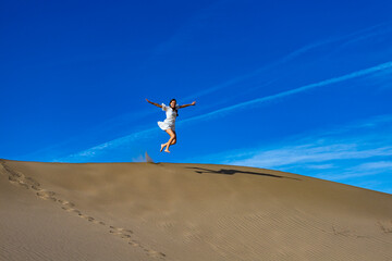 girl in white dress jumps on large sand dunes in mesquite flat sand dunes in death valley national park. Roadtrip in California, USA