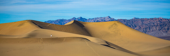 Fototapeta na wymiar girl in white dress lost in the desert; walking on large sand dunes in mesquite flat sand dunes in death valley national park, california, usa